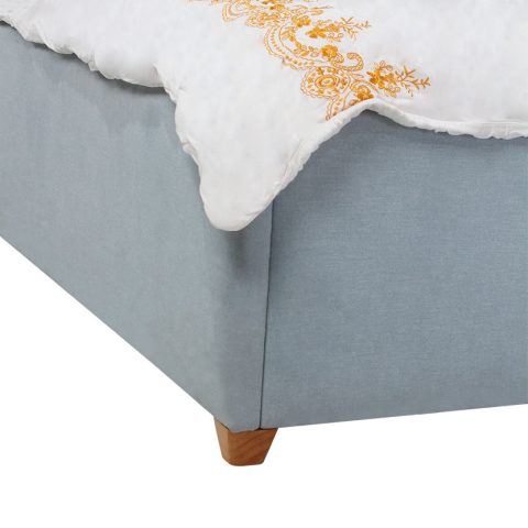 Cận cảnh chân giường gỗ hình khối vát cạnh, nâng đỡ khung giường bọc vải