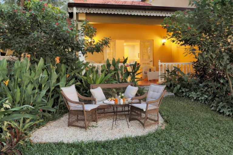 Bộ bàn ghế mây ngoài trời đặt trong sân vườn xanh, không gian ấm cúng trước hiên nhà