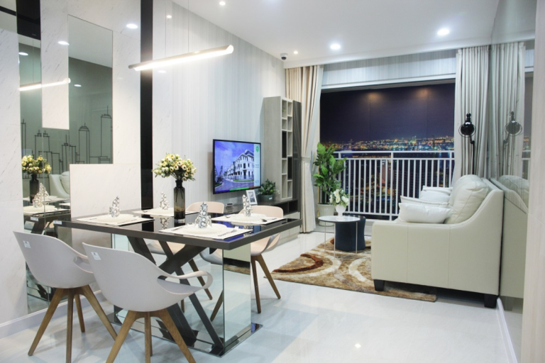 Không gian hiện đại với bàn ăn mặt kính, ghế nhựa chân gỗ, sofa sáng màu và ban công căn hộ.