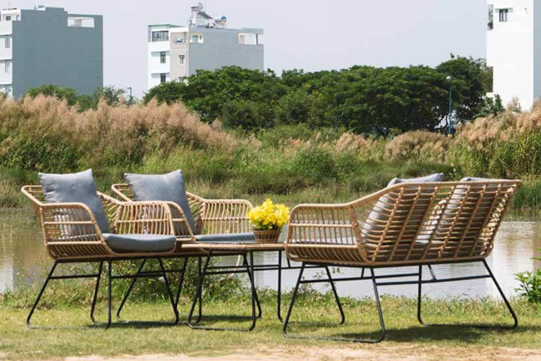 Bộ bàn ghế mây nhựa Basil gồm ghế và bàn trà, đặt ngoài trời bên hồ nước với nền cỏ và khung cảnh cây xanh xung quanh.