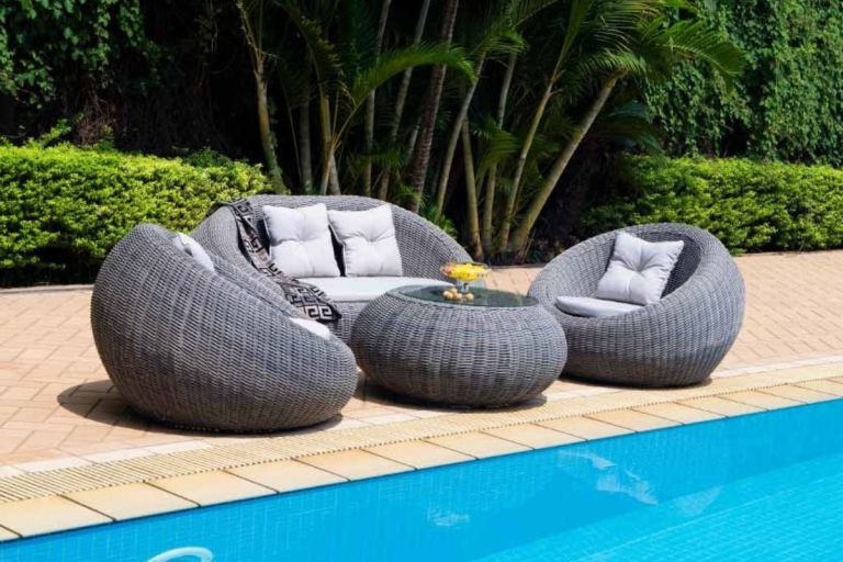 Bộ bàn ghế mây nhựa Coconut với thiết kế bo tròn gồm ghế đôi, ghế đơn và bàn, đặt cạnh hồ bơi trong không gian xanh mát.