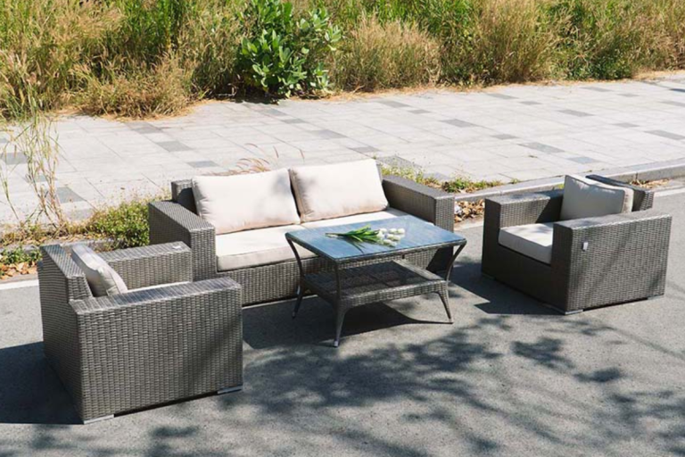 Bộ bàn ghế mây nhựa Cubana gồm sofa băng đôi, hai ghế đơn và bàn trà, đặt tại không gian ngoài trời với nền lát gạch và cây xanh xung quanh.